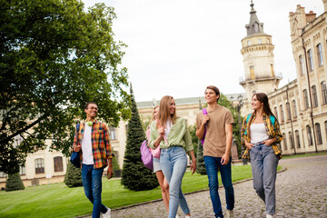 Fototapeta premium Group of university students walking and laughing together on a historic campus lawn with backpacks and casual clothes