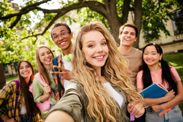 Obraz premium Smiling college students taking a selfie together on campus with backpacks and notebooks, diverse group of friends enjoying outdoor campus life and university social moments