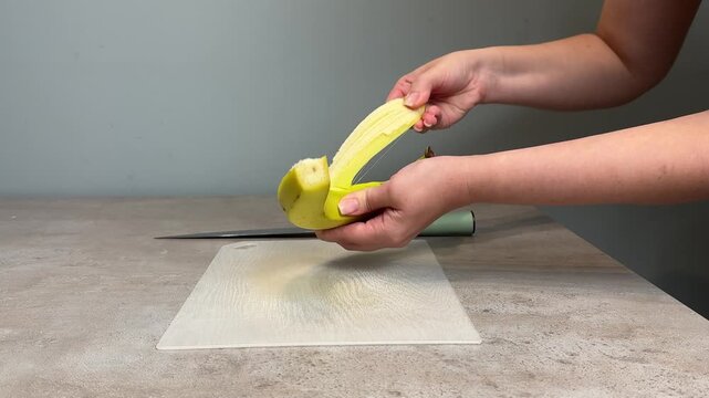 Hands peeling green banana over cutting board during midsequence kitchen preparation showing