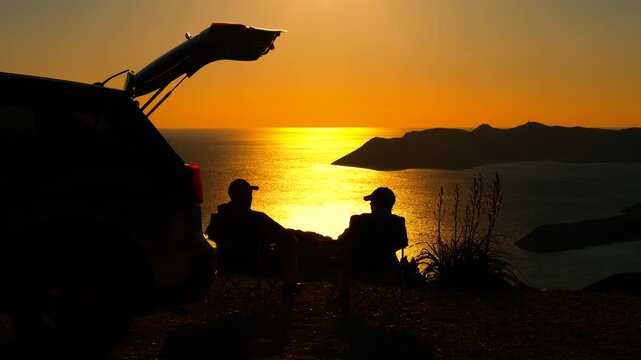 Two silhouetted men packing camping chairs after sunset. Two silhouetted men packing up their camping chairs next to a car with an open trunk after enjoying a stunning golden sunset over the ocean
