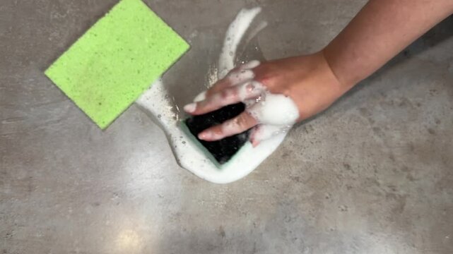 Midsequence topdown hand scrubbing soapy countertop with sponge showing dirt removal progress