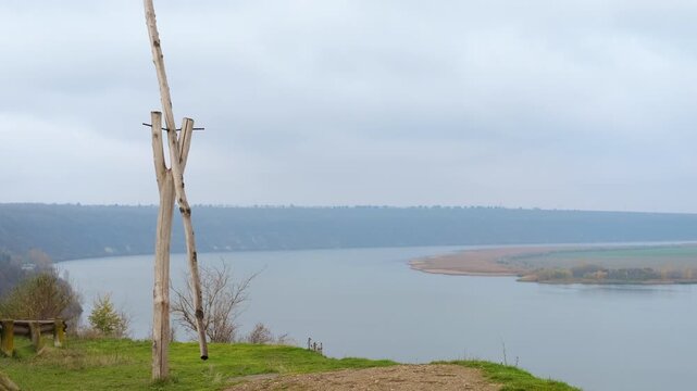 Wooden well sweep on a river bank in foggy weather. Melancholic view from a cliff with a traditional wooden well sweep overlooking a wide, calm river bend on an overcast, foggy autumn day