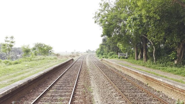 Smooth low-altitude drone footage flying rapidly forward, approximately one meter above parallel railway tracks through a peaceful rural landscape. 