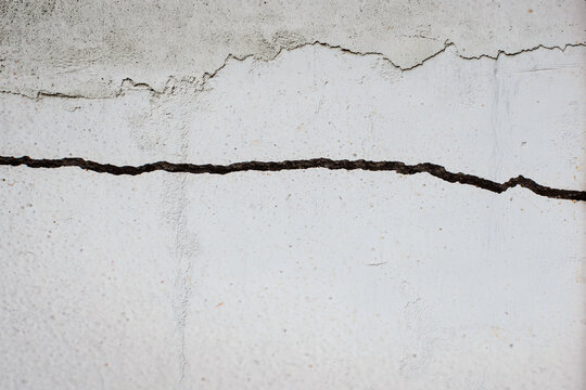 Damaged cracked concrete wall with patched old cracks.
