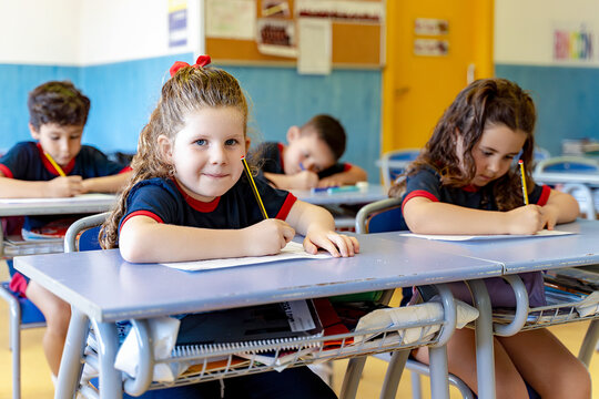 Young students in school uniform sitting at desks, writing on paper during an elementary education lesson