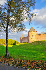 Obraz premium Autumn city landscape - towers and walls of Veliky Novgorod Kremlin on the hill framed by autumn trees under warm sunset light