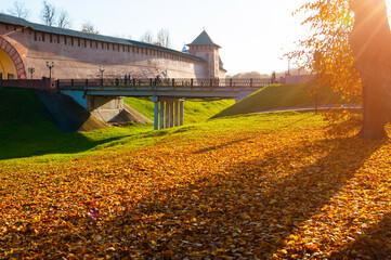 Veliky Novgorod, Russia. Veliky Novgorod Kremlin fortress, pedestrian bridge and bright orange fallen leaves on the ground in sunny autumn morning. Autumn city scene