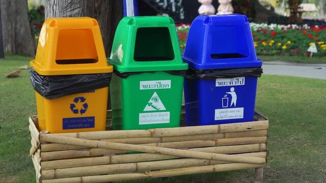 Brightly colored bins for different types of waste are arranged in a row on a grassy area, promoting environmental responsibility