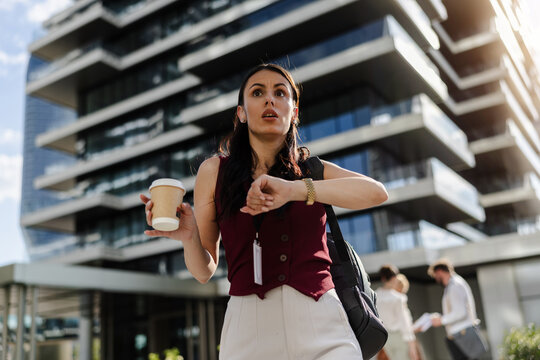 Professional woman checking watch while holding coffee outdoors