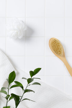 Top view of organic spa product mockup background with green leaves. Flat lay of body brush, bath puff, and white towel on square tile wall with copy space for cosmetic display.