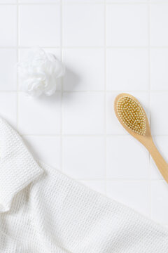 Top view of bathroom product mockup background with copy space. Flat lay of body brush, bath puff, and white towel on square tile wall for cosmetic display.