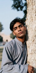Obraz premium Vertical outdoor portrait of young male leaning on tree in soft daylight for portrait background and editorial design