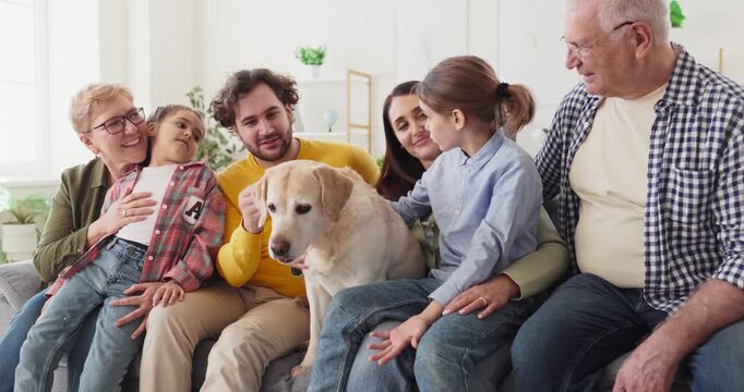 Family grandparents parents children bonding with labrador dog. They gather on the sofa at home, talking, smiling, and gently petting the calm pet together. Love unites generations at home.