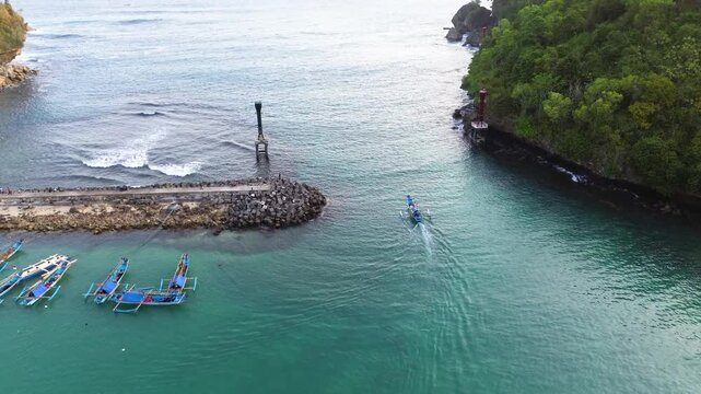 Aerial drone footage of a traditional fishing boat leaving the harbor pier and heading toward the open sea. Cinematic aerial perspective capturing the vessel departing from the dock