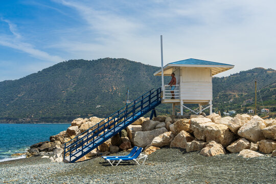 Male tourist standing in white beach lifeguard tower while looking across Mediterranean Sea in Pomos, Cyprus. Coastal scenery, leisure travel and relaxation concept.