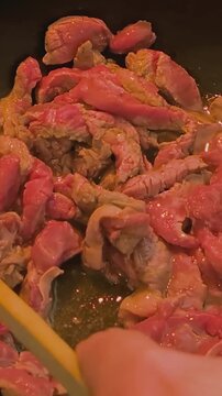 Frying pieces of meat in a pan while stirring over medium heat in a kitchen setting