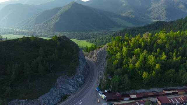 A cinematic drone revealing shot flying over a rocky mountain cleft to uncover a scenic asphalt road and a lush green valley at Chike-Taman Pass in Altai.