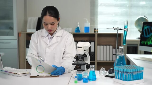 Asian scientist writing research data on a clipboard in a laboratory, medical scientist analyzing sample results for drug discovery in a modern scientific lab with a microscope