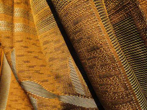 Close‑up of folded golden‑brown woven songket fabric with intricate pattern