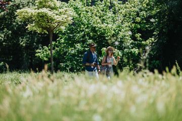 Fototapeta premium A couple of tourists walk through a sunlit park holding a map and drinking water. The pair stroll together in a leafy green setting while exploring outdoors.