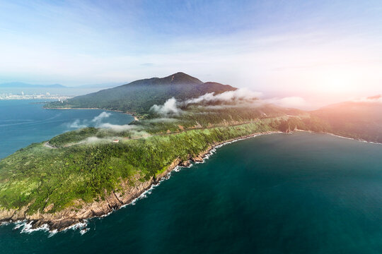Lush green jungle covers the Son Tra Peninsula mountains, reaching a rocky coast where waves meet the deep blue ocean. Clouds drift over peaks