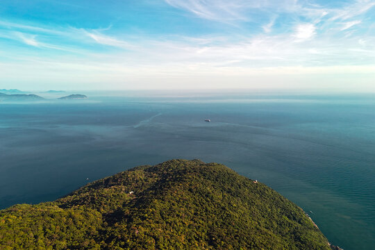 An aerial perspective reveals Son Tra Peninsula's vibrant jungle descending to the tropical ocean in Da Nang, Vietnam. A lone ship crosses the calm waters