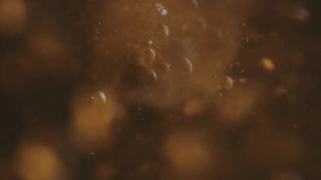 Golden effervescent bubbles rising in amber liquid, macro carbonated beverage texture, sparkling soda or beer close up with soft bokeh
