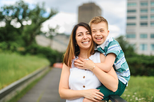 cute little child with trisomy 21 syndrome outside in summer season with his mother