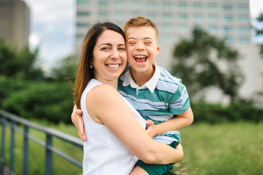 cute little child with trisomy 21 syndrome outside in summer season with his mother