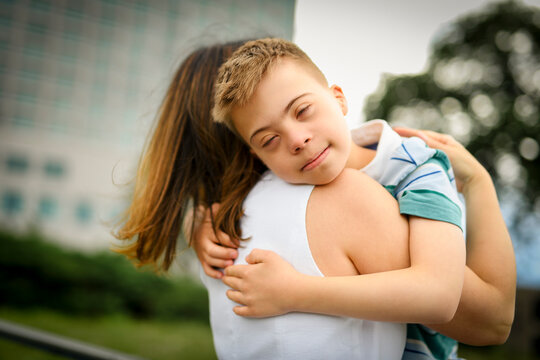 cute little child with trisomy 21 syndrome outside in summer season with his mother