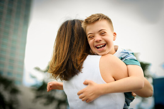 cute little child with trisomy 21 syndrome outside in summer season with his mother