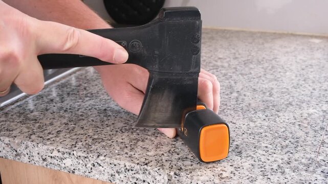 Close-up of a man sharpening a small hatchet with a manual sharpener. Tool maintenance for woodworking, camping, survival, home improvement and safety