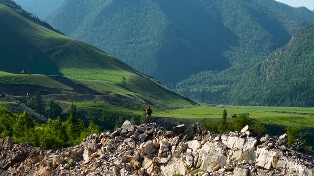 A cinematic wide shot with a drone flying backward and ascending to reveal a vast Altai mountain landscape as a lone male explorer stands on top of a rocky cliff.