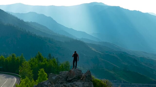 Cinematic 360-degree drone orbit flight focused on a male tourist standing on a high rocky ledge at Chike-Taman Pass.