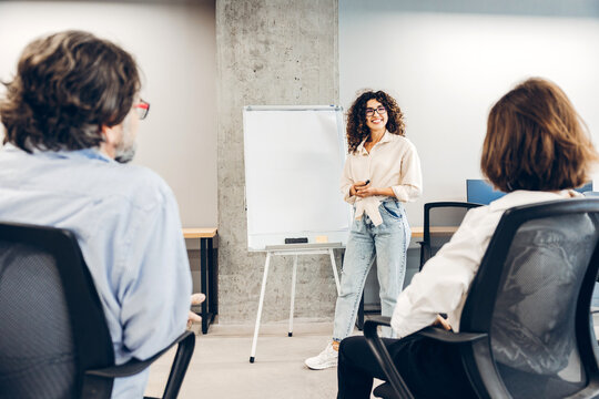 Smiling woman with curly hairstyle and eyeglasses presenting business strategy at office meeting