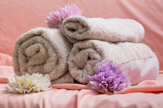 Rolled towels next to flowers on a pink sheet in a spa setting. Concept of relaxation, wellness, self care, harmony, rest, and beauty