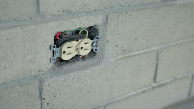 Close-up of a NEMA 5-15R Duplex Electrical Receptacle with Exposed Wiring Installed in a Concrete Block Wall