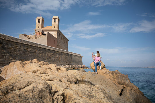 Middle aged mother and her teenage son taking a selfie on the rocky coastline of Tabarca beside the historic church during a summer family vacation