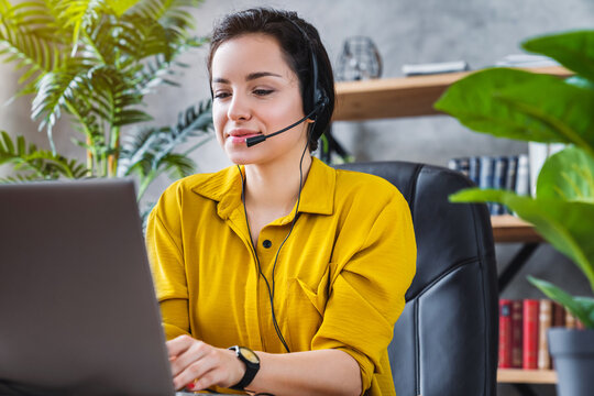 Beautiful female freelancer talking in online video conference using headset with microphone and laptop in home office, remote work and communication concept