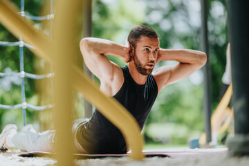 Fototapeta premium A fit young man performs abdominal crunches on a mat with his hands behind his head. He trains core muscles outdoors in a focused workout session.
