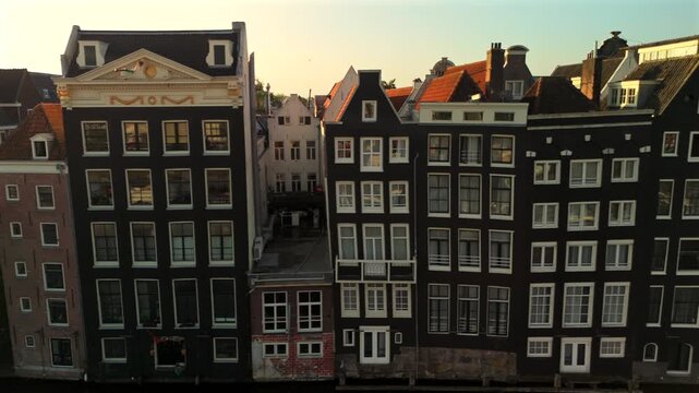 Drone moves rightward past a row of iconic Amsterdam canal houses with diverse gabled facades and brick architecture