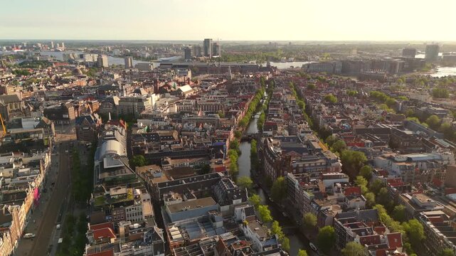 Forward aerial drone flies above central Amsterdam revealing tree lined canals the city horizon and IJ waterway