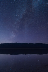 Fototapeta premium Sierra Nevada mountain silhouette under starry night sky with Milky Way reflection on calm water