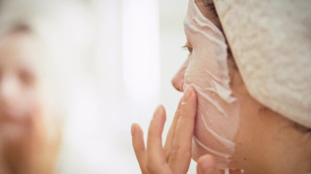 A woman gently presses an aloe vera sheet mask onto her face, smoothing it for a snug fit. The home skincare ritual delivers intensive moisture and nourishment, highlighting modern facial care