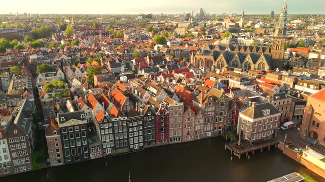 Drone flies leftward above Amsterdam waterfront revealing the Oude Kerk church and classic canal house facades below