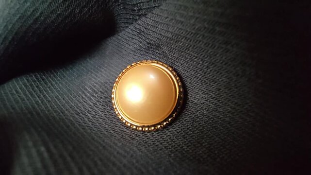 Elegant macro close-up of a luxurious cream pearl button with a decorative gold frame, set against a dark textured fabric background, ideal for fashion design, formal wear, and high-end clothing detai