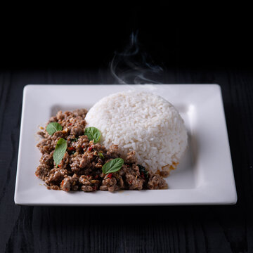 Spicy Thai pad kra pao with ground beef and hot jasmine rice on white plate.