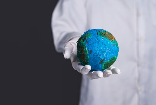 Robot hand holding a small planet earth globe on dark background.