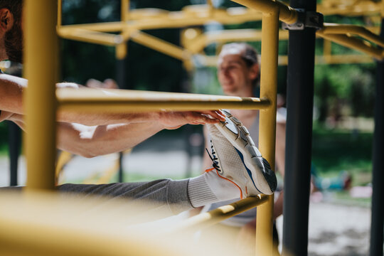 Man stretching his leg on yellow outdoor gym bars while another person watches in soft focus. A close-up shows a sneaker foot resting on the parallel bars during an outdoor workout.