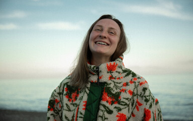 Smiling young woman in floral fleece jacket standing on beach at sunset © Pavel